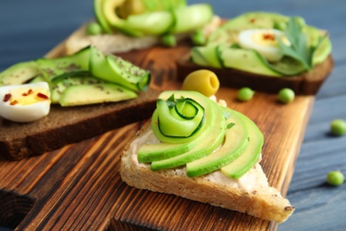 Photo of Crisp toasts with sliced avocado and cream cheese on wooden board, closeup