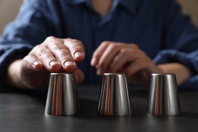 Woman playing thimblerig game with metal cups at black table, closeup