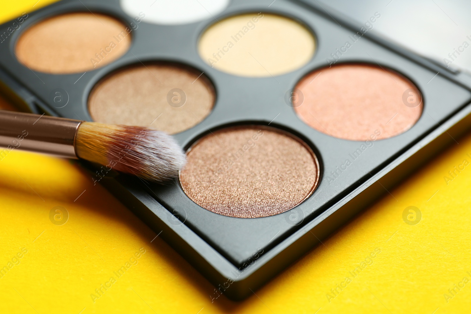 Photo of Eye shadow palette with professional makeup brush on yellow background, closeup