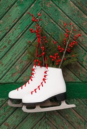 Photo of Pair of ice skates with Christmas decor hanging on green wooden wall