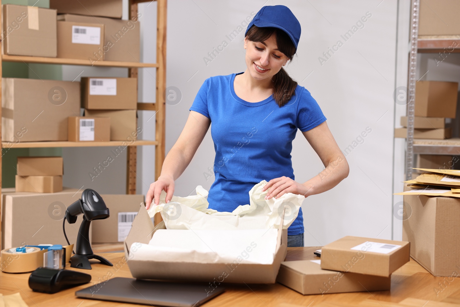 Photo of Post office worker packing parcel at wooden table indoors