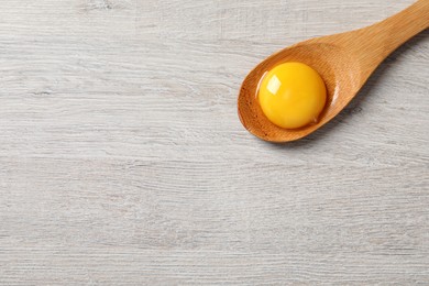 Photo of Spoon with raw egg yolk on white wooden table, top view. Space for text