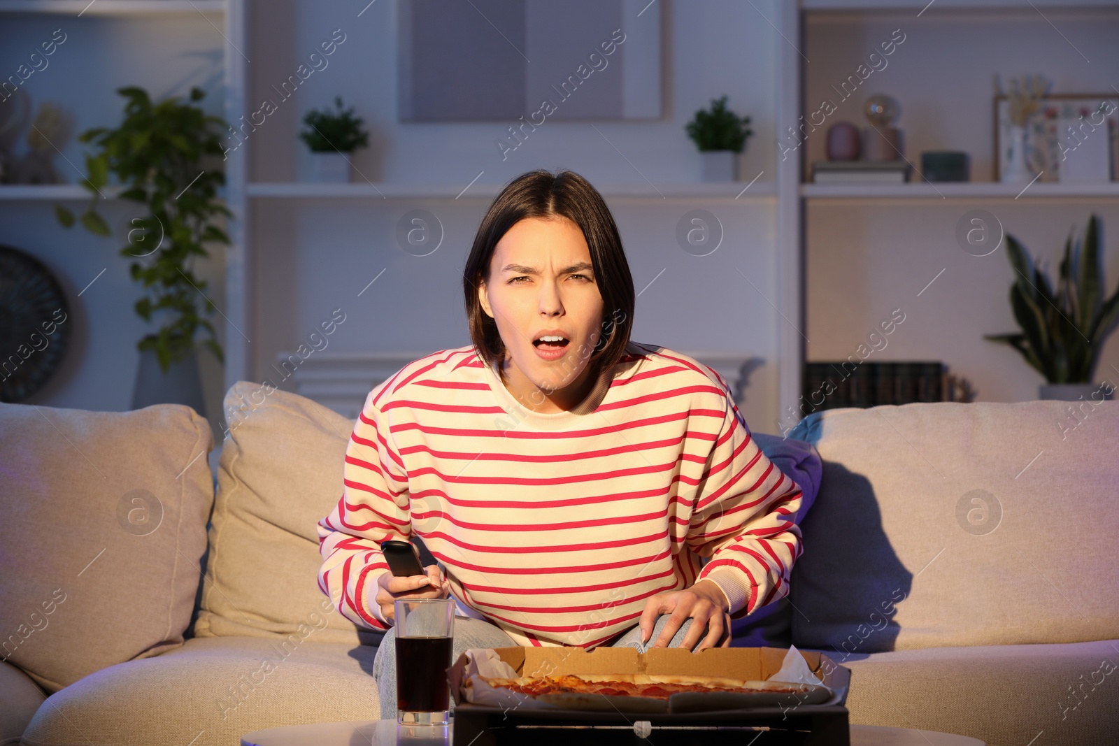 Photo of Emotional woman watching TV with pizza on sofa at home