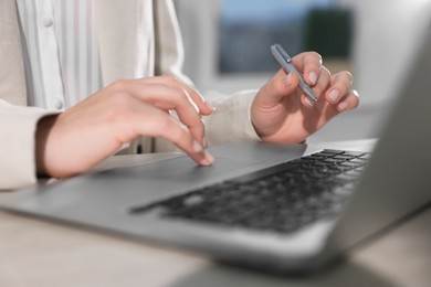 Woman with pen working on laptop at wooden table, closeup. Electronic document management