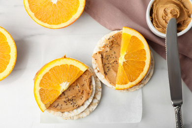 Puffed rice cakes with peanut butter and orange on white marble table, flat lay