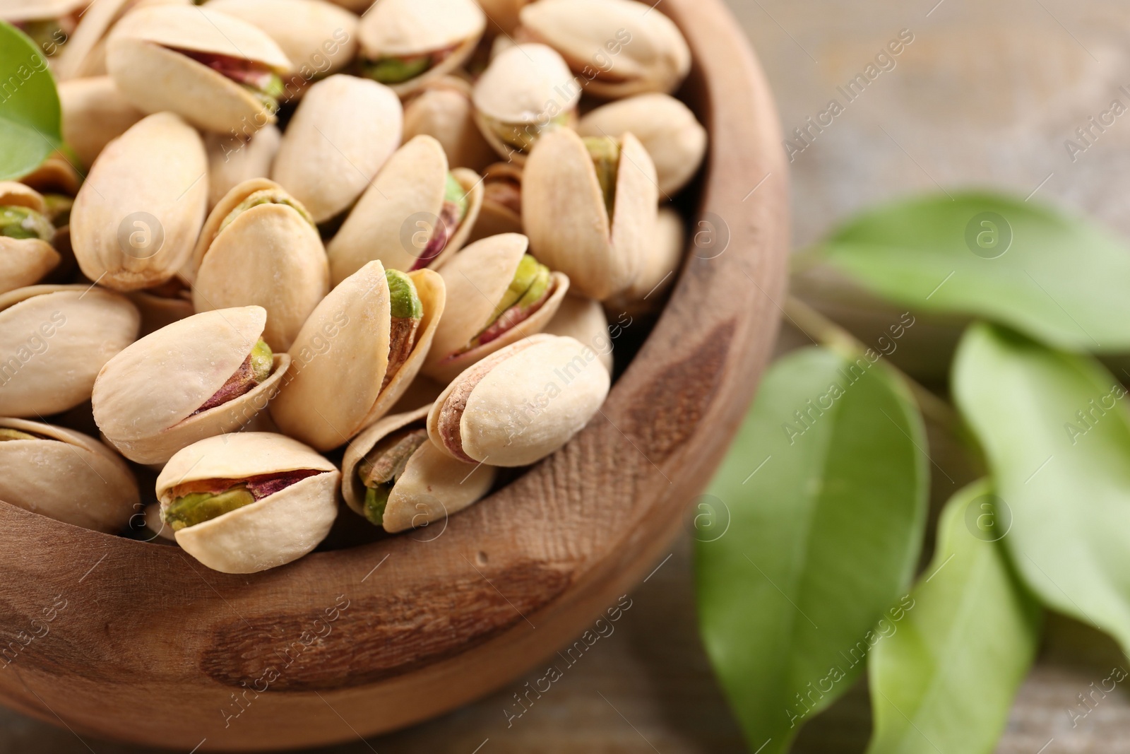 Photo of Delicious pistachios in bowl on wooden table, closeup