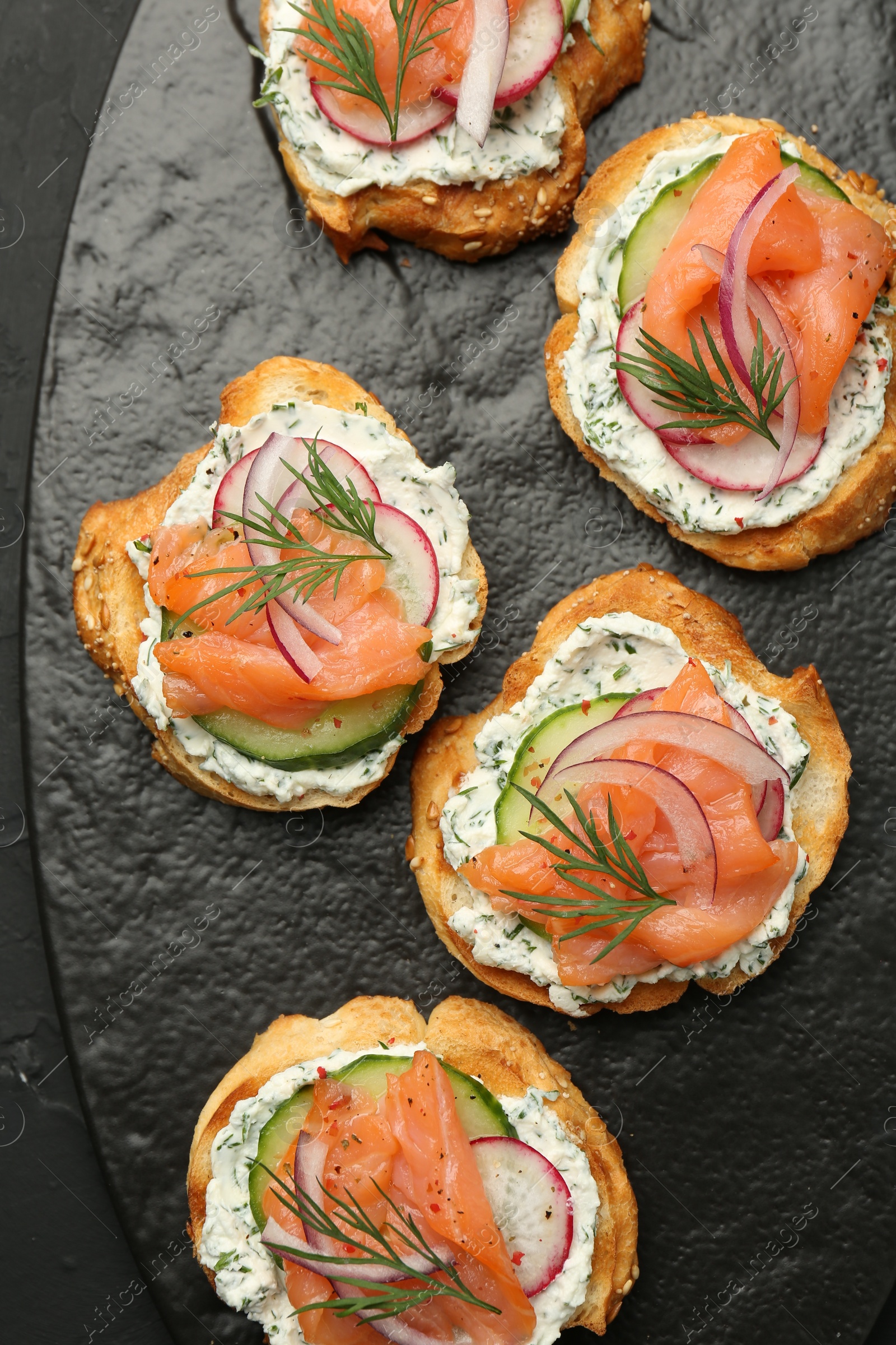 Photo of Tasty canapes with salmon, cucumber, radish and cream cheese on black table, top view