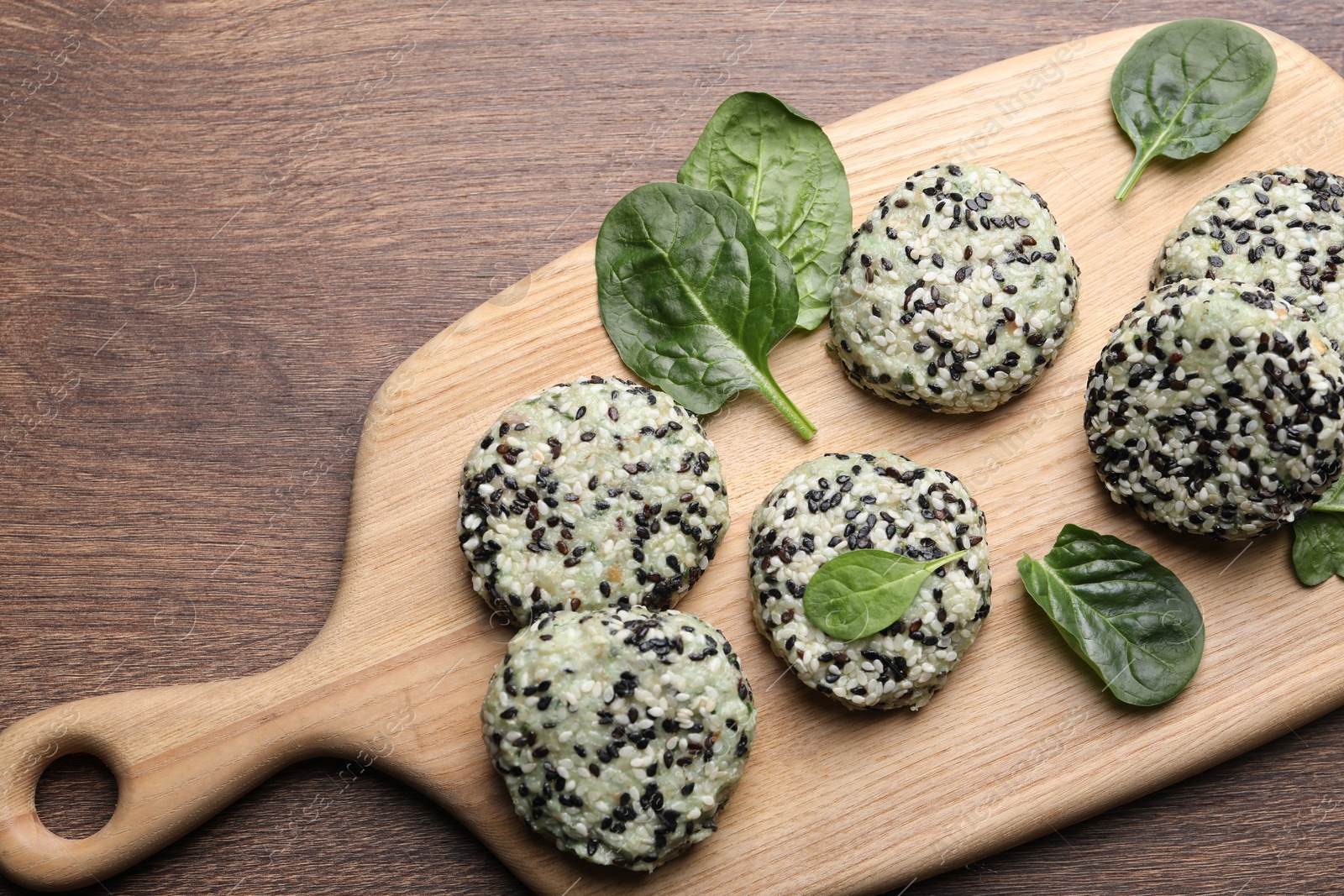 Photo of Tasty vegan cutlets with sesame seeds and spinach on wooden table, top view