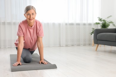Photo of Senior woman in sportswear stretching on fitness mat at home, space for text