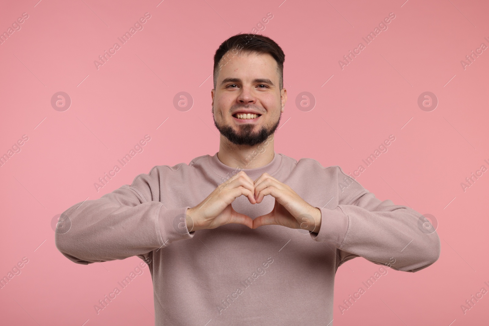 Photo of Man showing heart gesture with hands on pink background