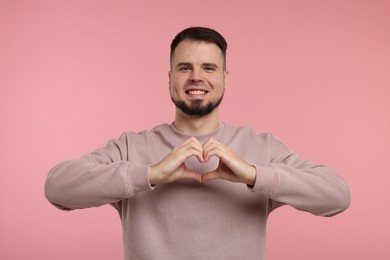 Man showing heart gesture with hands on pink background