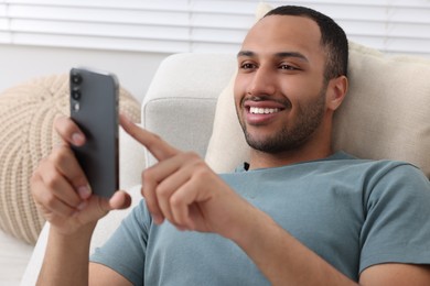 Happy man sending message via smartphone indoors