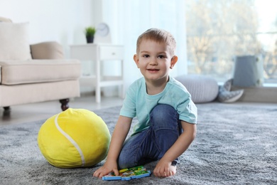 Photo of Cute child playing with soft toy on floor indoors