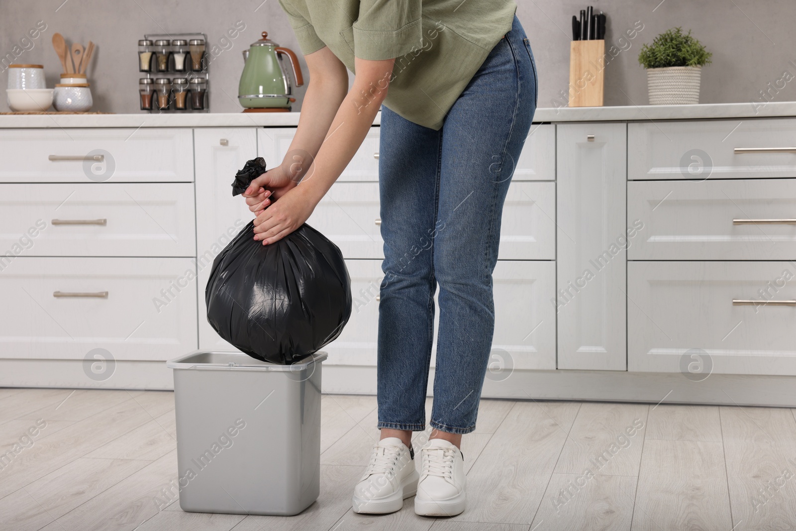 Photo of Woman taking garbage bag out of trash bin in kitchen, closeup