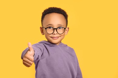 African-American boy with glasses showing thumb up on yellow background