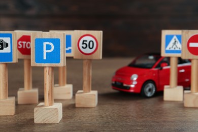 Photo of Many different miniature road signs and car on wooden table. Driving school