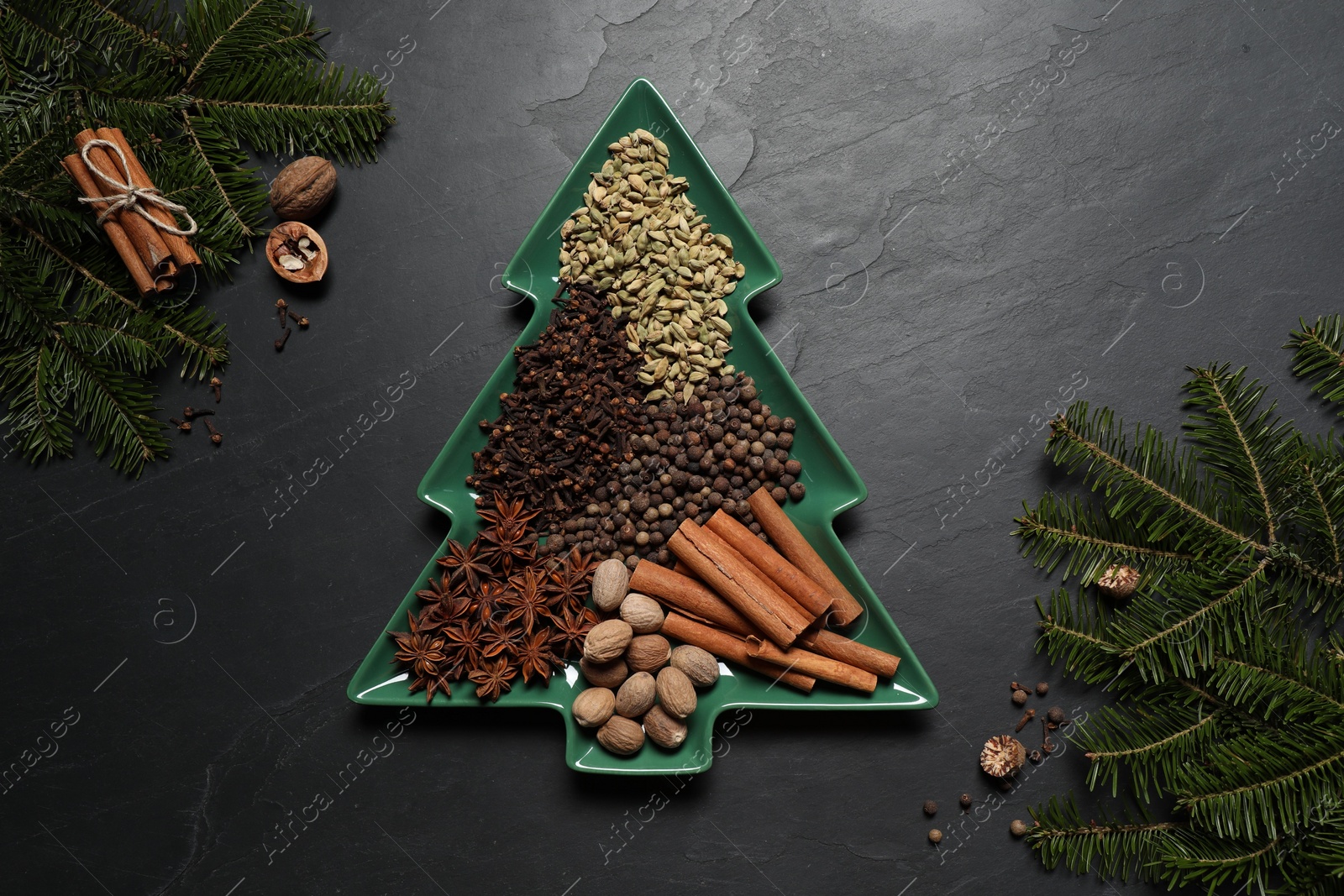 Photo of Different spices, nuts and fir branches on dark gray textured table, flat lay