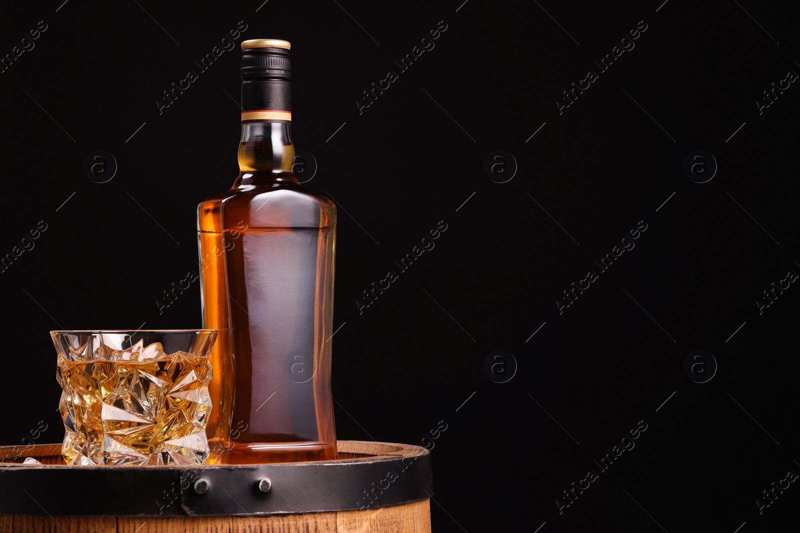 Photo of Whiskey in glasses and bottle on wooden barrel against black background, space for text