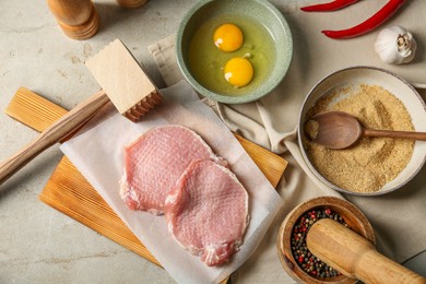 Raw pork chops, meat mallet and ingredients for cooking schnitzel on grey table, flat lay