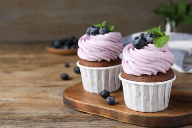 Photo of Sweet cupcakes with fresh blueberries on wooden table. Space for text