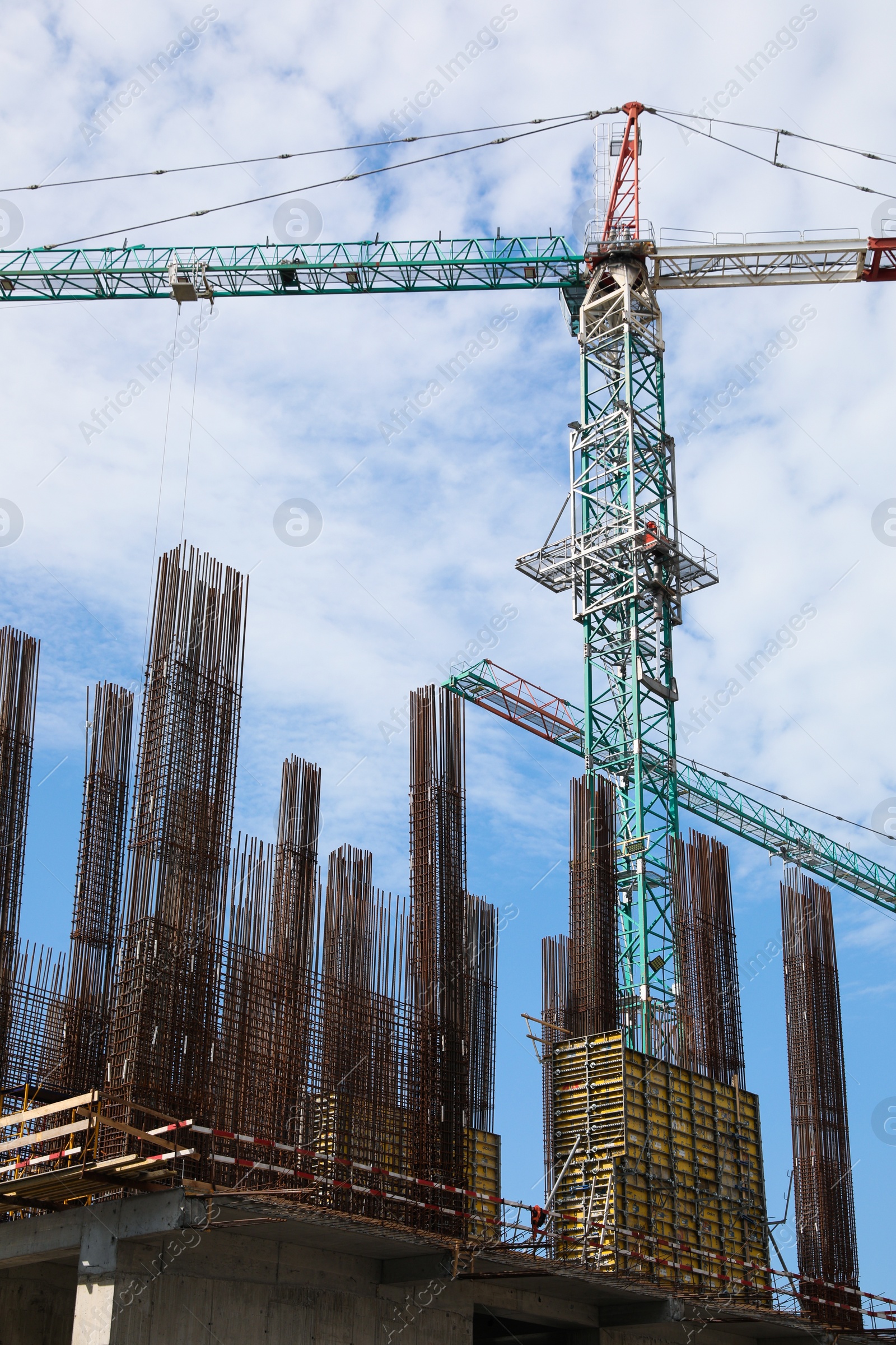 Photo of Tower crane near building under construction against cloudy sky