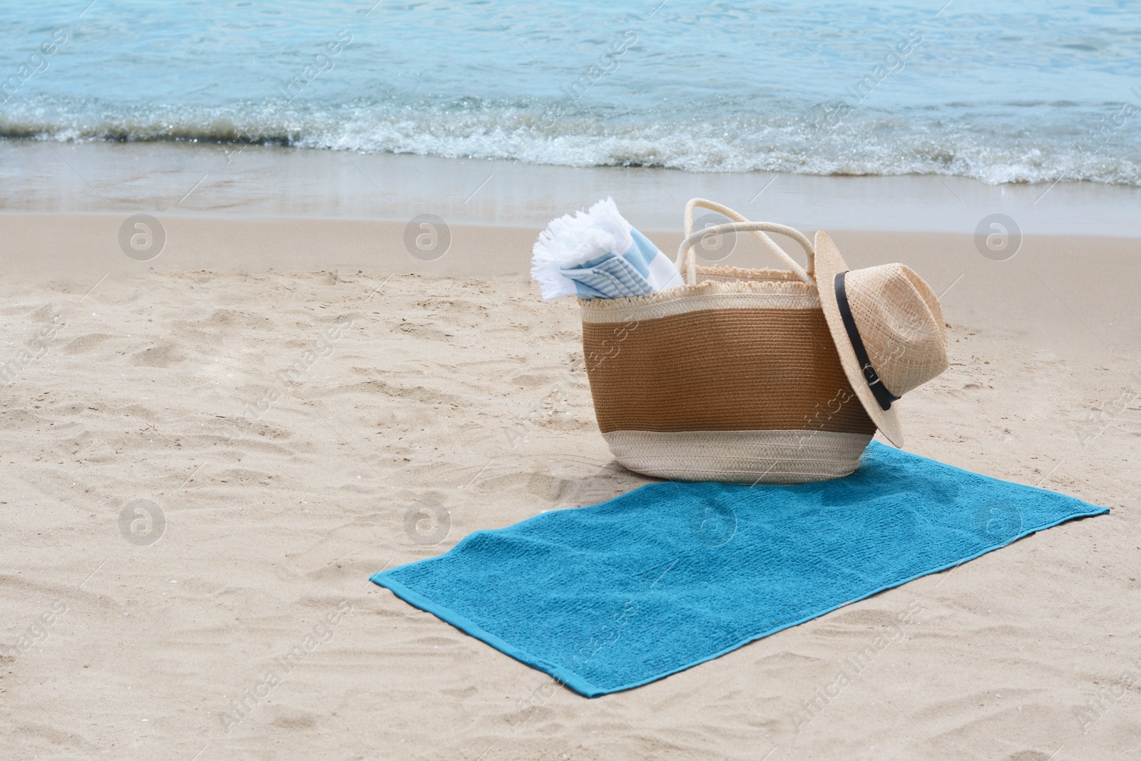 Photo of Bag with blanket, beach towel and straw hat on sandy seashore, space for text