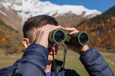 Photo of Boy looking through binoculars in mountains on sunny day
