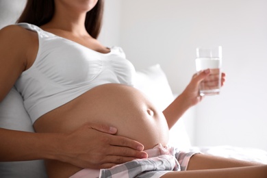 Photo of Young pregnant woman with glass of water in bedroom, closeup. Taking care of baby health