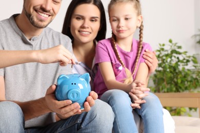 Photo of Happy family putting coin into piggy bank at home, closeup