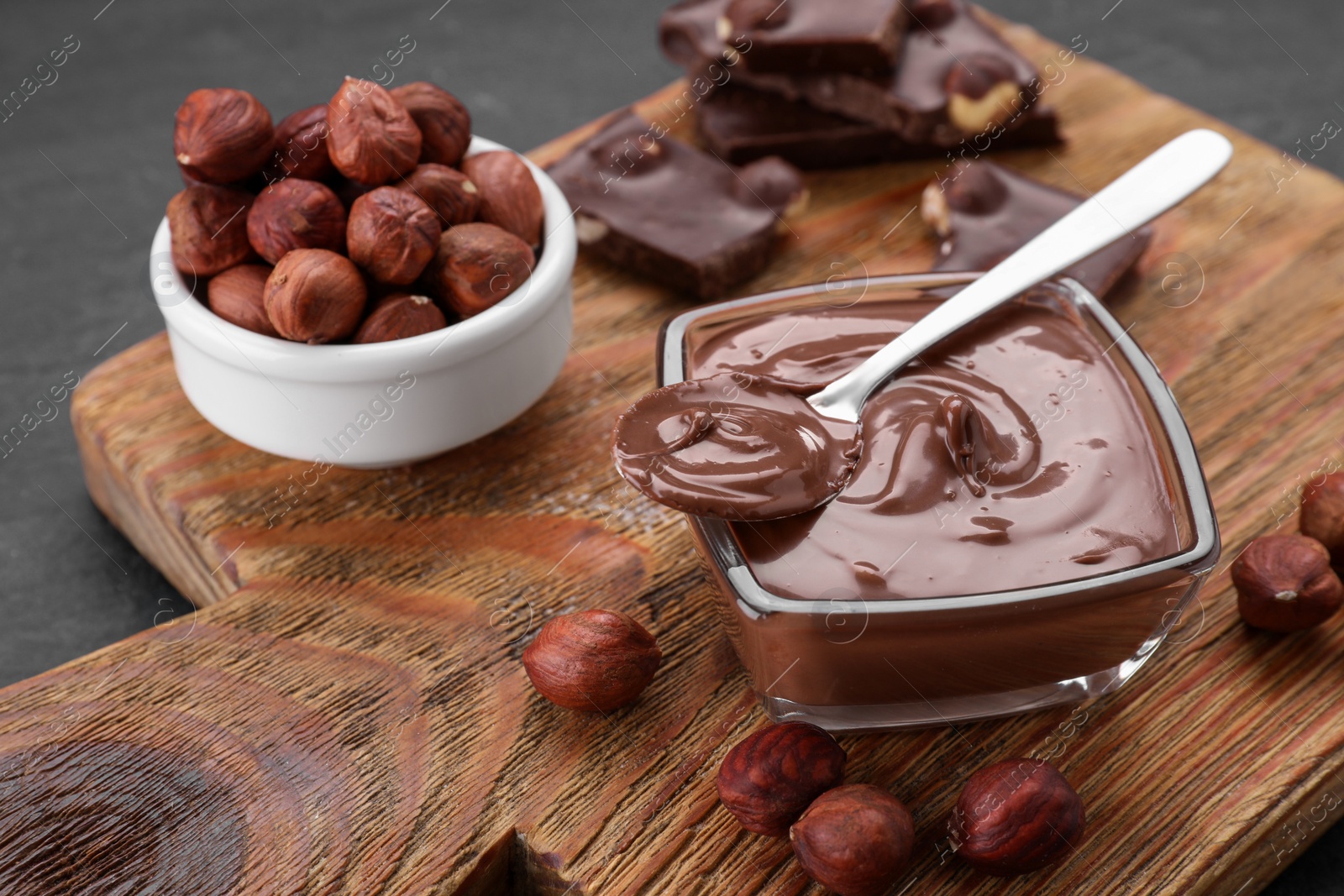 Photo of Bowl with tasty paste, chocolate pieces and nuts on wooden board, closeup