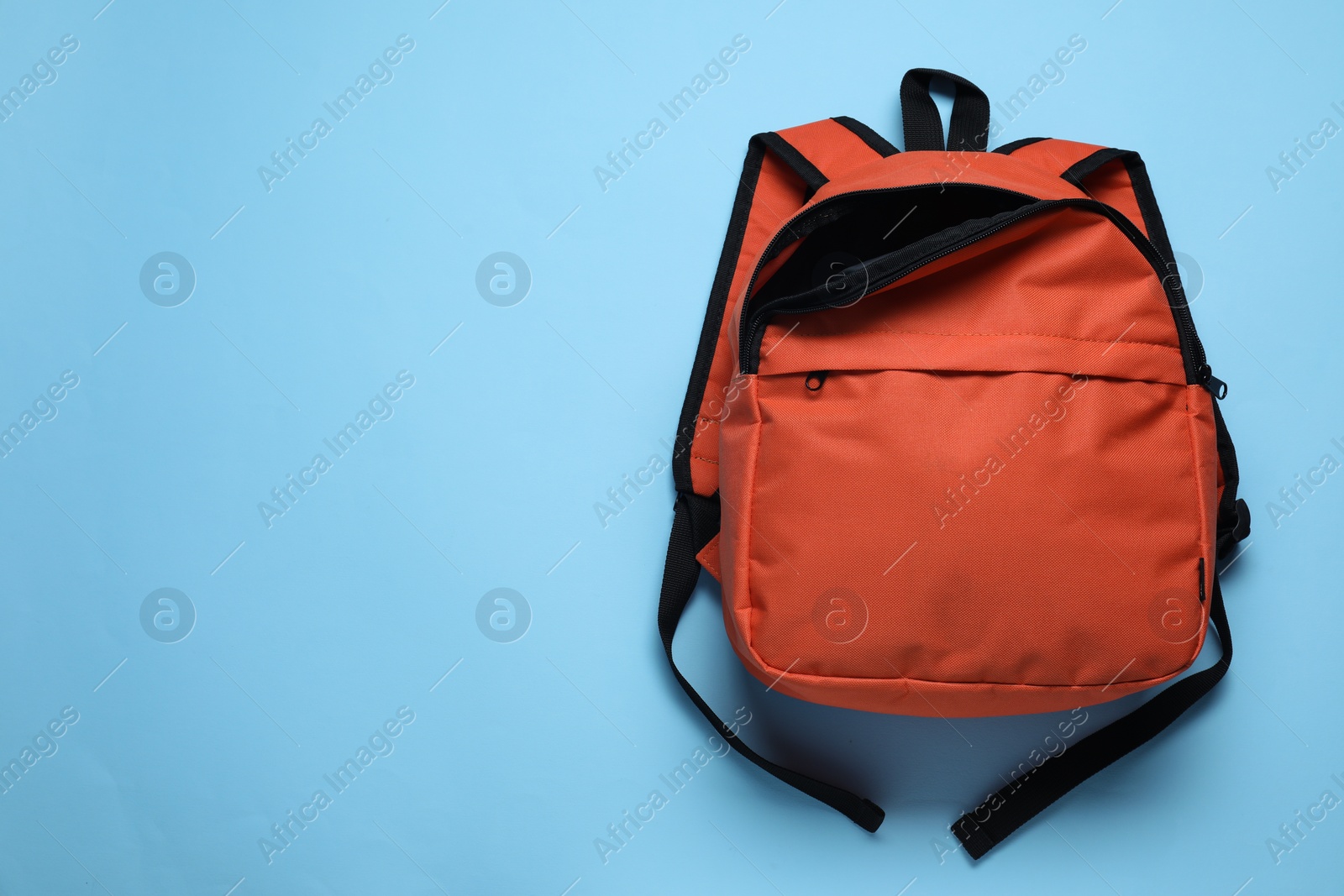 Photo of Stylish orange backpack on light blue background, top view. Space for text