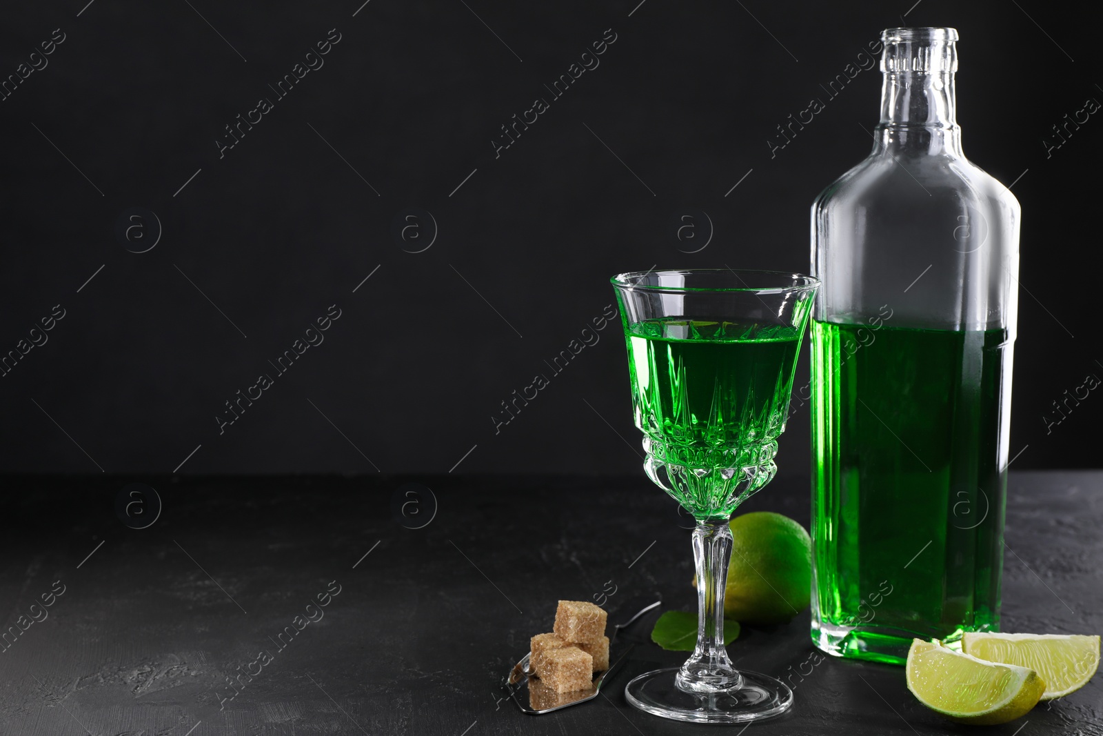 Photo of Absinthe, spoon, brown sugar and lime on black table, space for text. Alcoholic drink