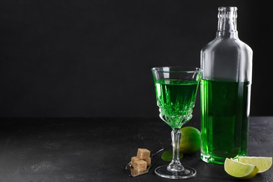 Photo of Absinthe, spoon, brown sugar and lime on black table, space for text. Alcoholic drink