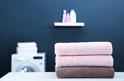 Photo of Stack of clean towels on table in laundry room. Space for text