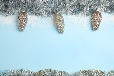 Shiny silver tinsel, snow and Christmas baubles on light blue background, flat lay. Space for text