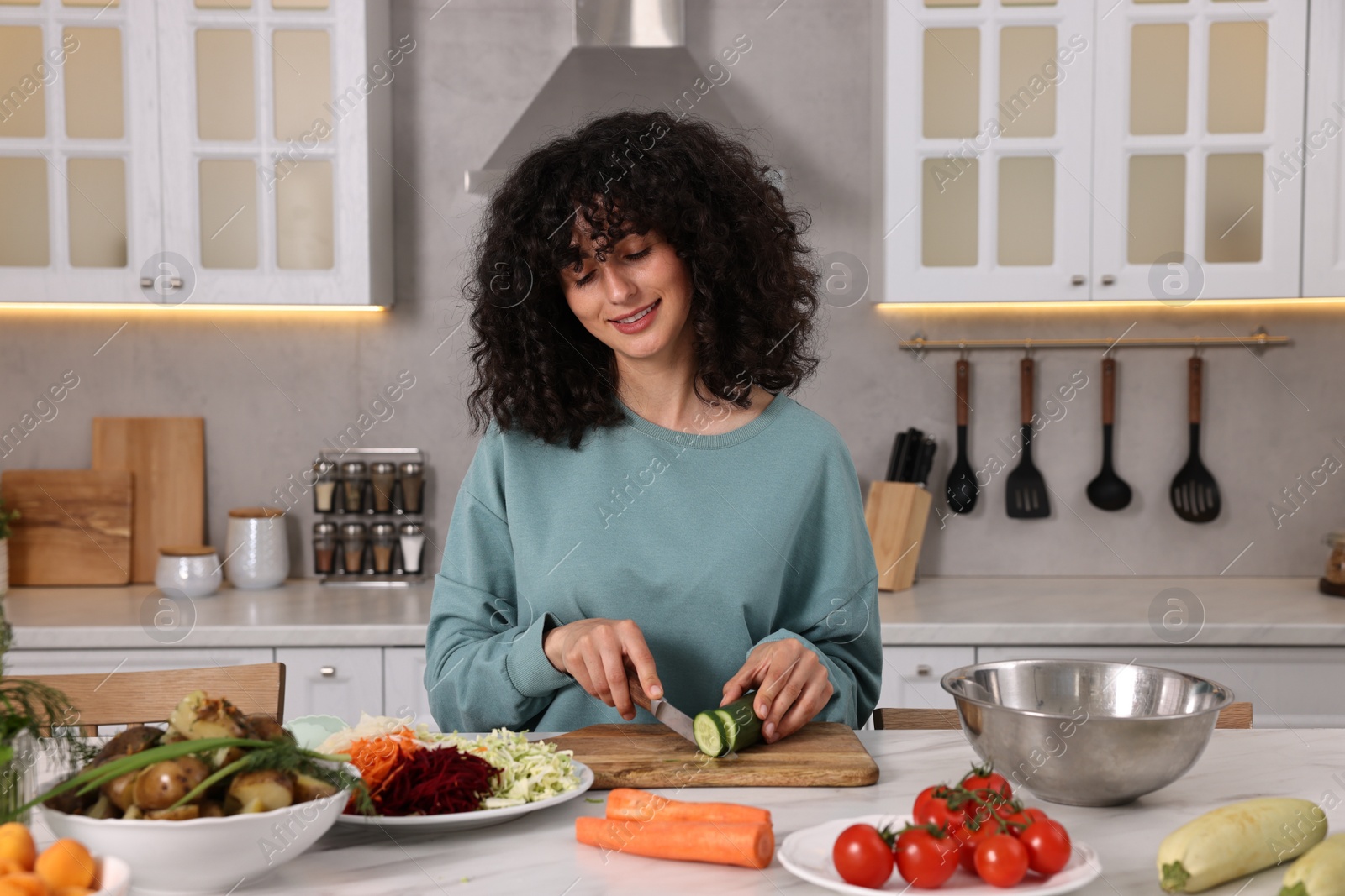 Photo of Woman cooking healthy vegetarian meal at white marble table in kitchen