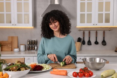 Photo of Woman cooking healthy vegetarian meal at white marble table in kitchen