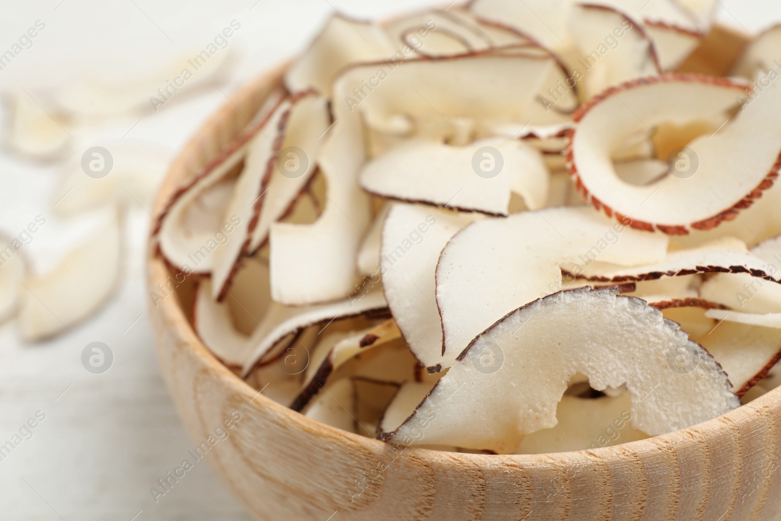 Photo of Tasty coconut chips in wooden bowl, closeup