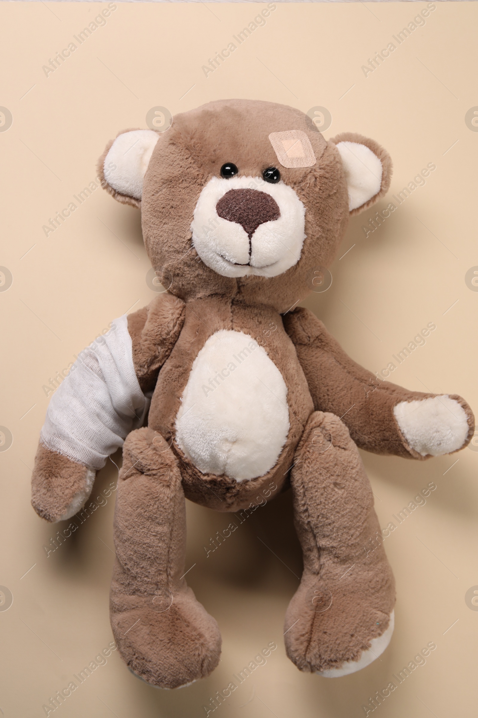 Photo of Toy bear with bandage on beige background, top view