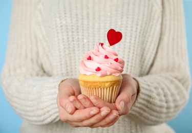 Photo of Woman holding tasty cupcake for Valentine's Day on light blue background, closeup