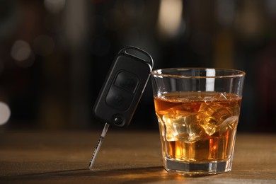 Photo of Car key and glass of alcoholic drink on wooden table against blurred background, space for text. Drunk driving concept