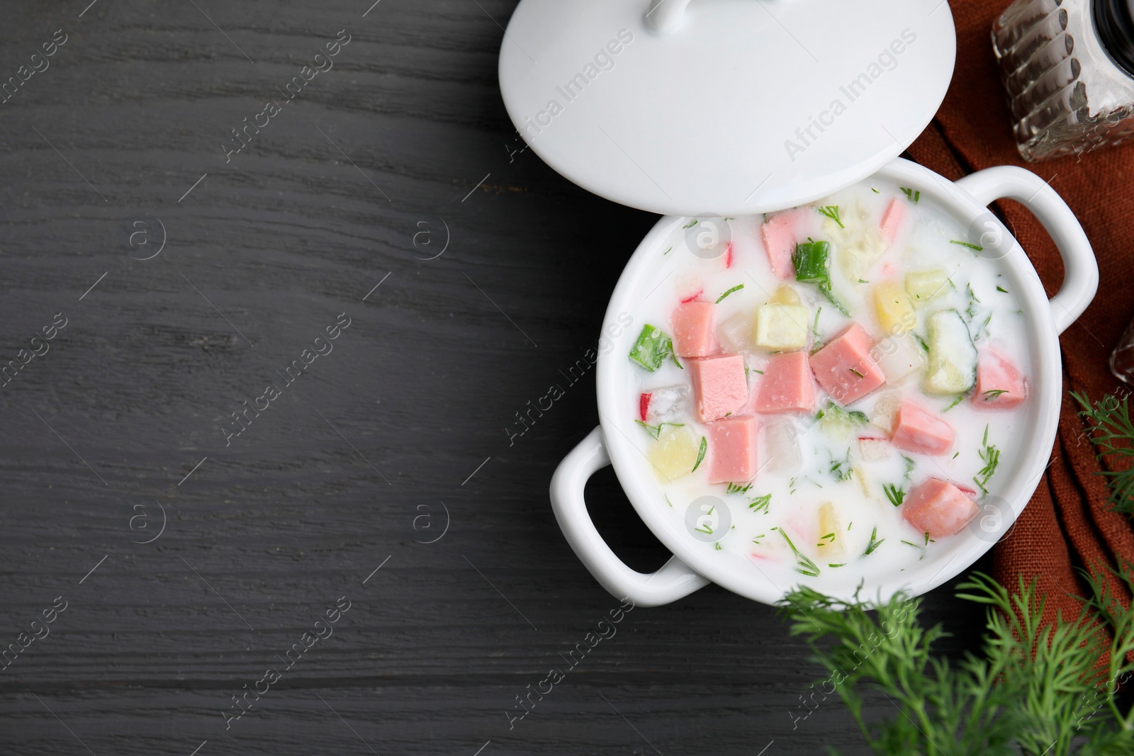 Photo of Delicious cold summer soup (okroshka) with boiled sausage in pot on grey wooden table, top view. Space for text