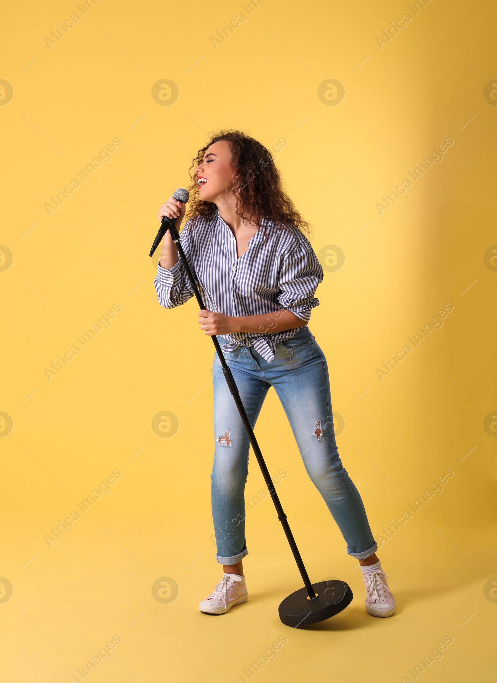 Photo of Curly African-American woman singing in microphone on color background