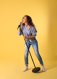 Curly African-American woman singing in microphone on color background