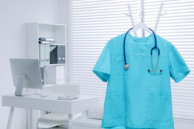 Photo of Turquoise medical uniform and stethoscope hanging on rack in clinic. Space for text