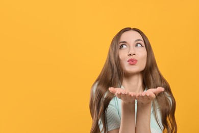 Photo of Beautiful young woman blowing kiss on yellow background, space for text