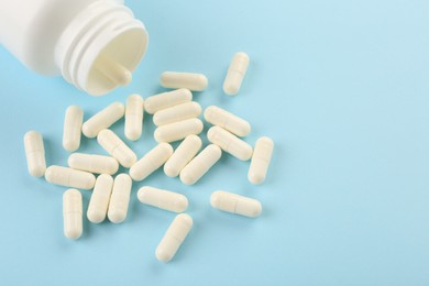 Bottle and vitamin capsules on light blue background, closeup. Space for text