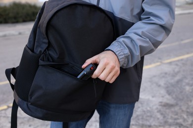 Photo of Man putting pepper spray into backpack outdoors, closeup