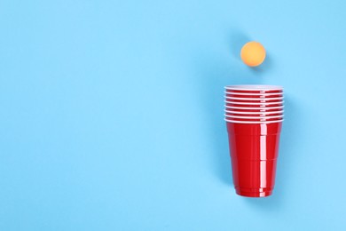 Photo of Plastic cups and ball on light blue background, flat lay with space for text. Beer pong game