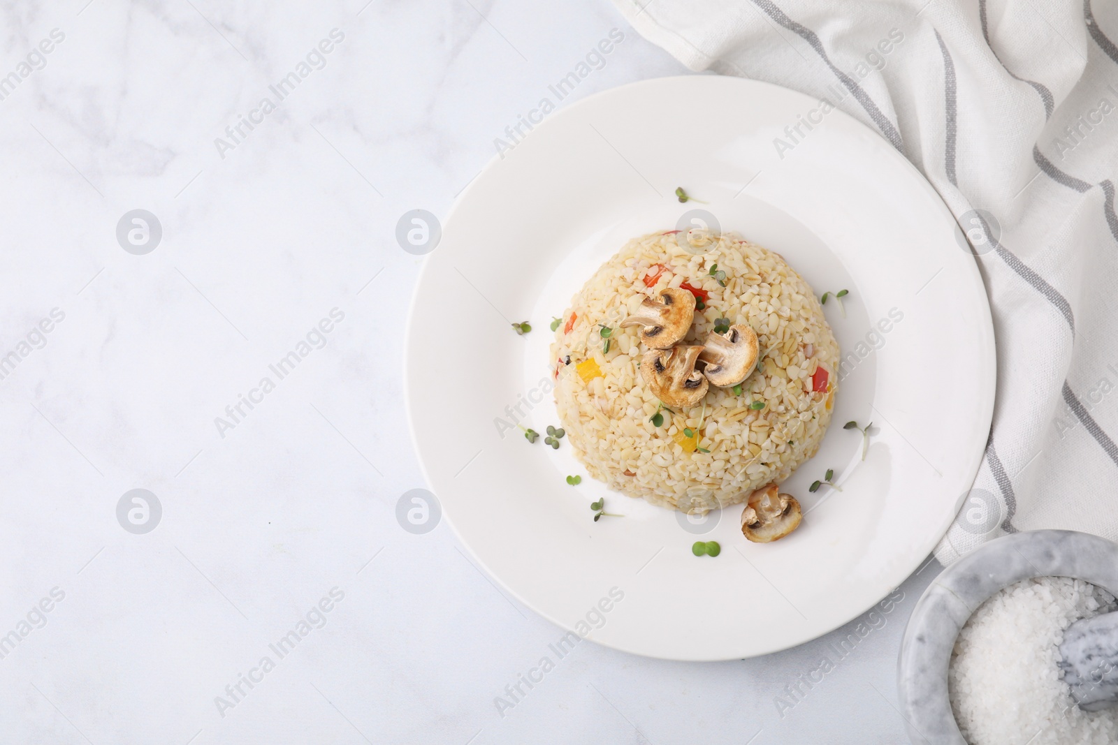 Photo of Delicious bulgur with vegetables, mushrooms and salt on white table, flat lay. Space for text